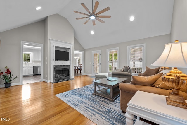 living room featuring baseboards, a ceiling fan, light wood finished floors, and high vaulted ceiling