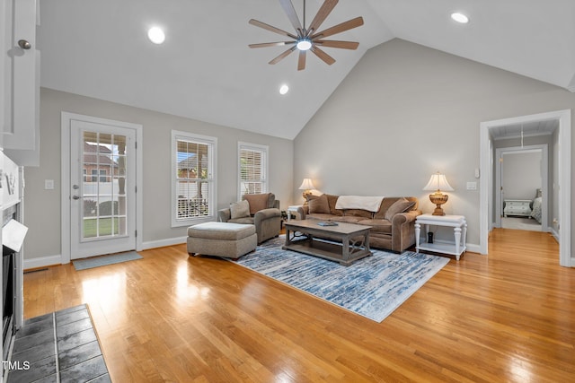 living area featuring light wood-type flooring, a fireplace with flush hearth, ceiling fan, and attic access