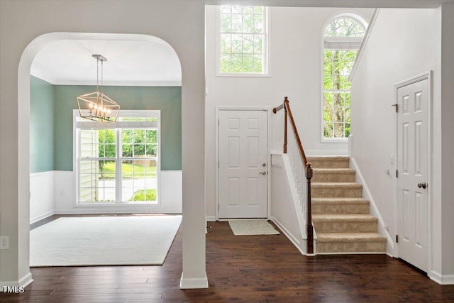 foyer entrance featuring baseboards, arched walkways, dark wood finished floors, and a notable chandelier