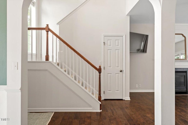 stairway with arched walkways, baseboards, and wood finished floors