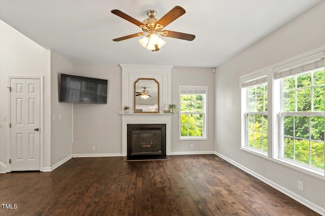 unfurnished living room with dark wood-type flooring, a fireplace with flush hearth, ceiling fan, and a wealth of natural light