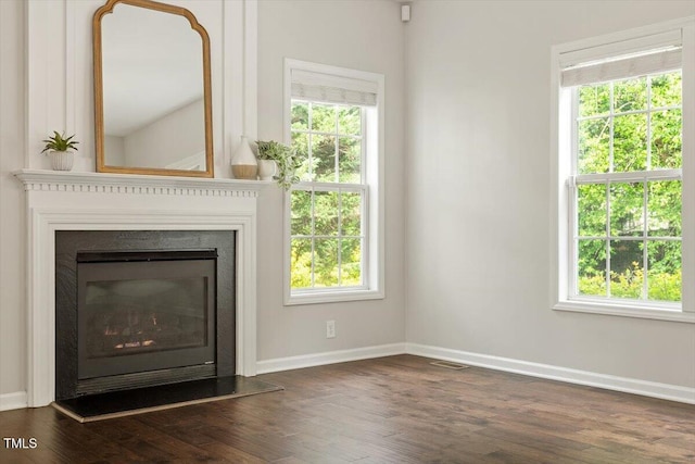 unfurnished living room with baseboards, dark wood-style floors, and a wealth of natural light