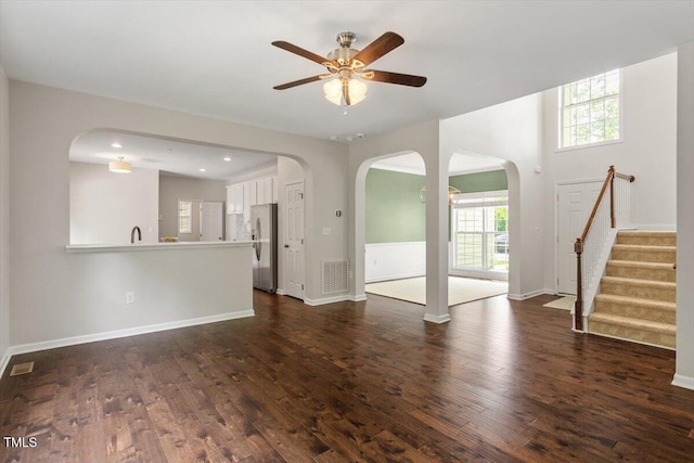 unfurnished living room with a ceiling fan, baseboards, dark wood finished floors, and visible vents