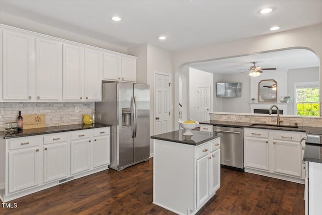 kitchen with white cabinets, appliances with stainless steel finishes, a sink, arched walkways, and a ceiling fan