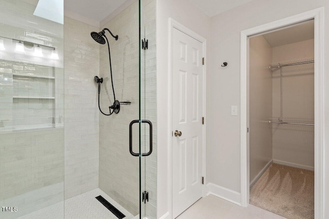 bathroom with baseboards, a shower stall, a walk in closet, and tile patterned flooring