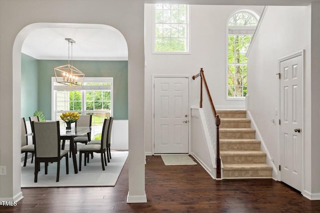 foyer entrance featuring arched walkways, baseboards, dark wood-type flooring, and a notable chandelier