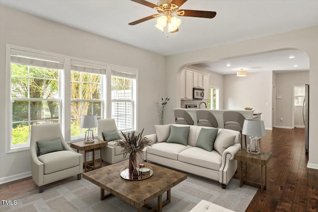 living room featuring arched walkways, baseboards, ceiling fan, and light wood finished floors