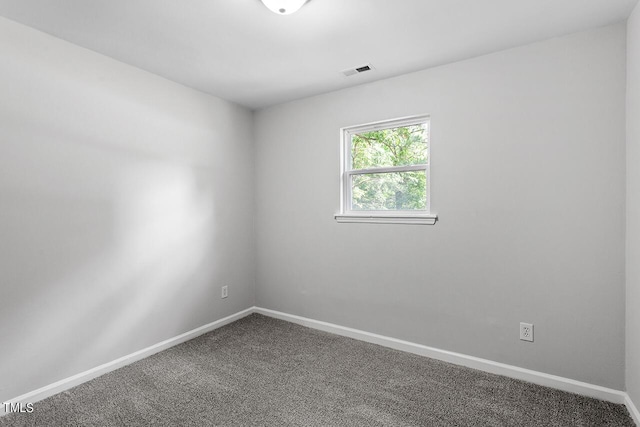 spare room featuring dark colored carpet, visible vents, and baseboards