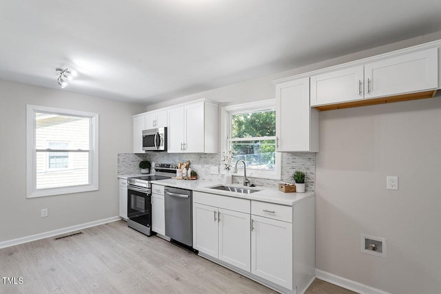 kitchen with tasteful backsplash, stainless steel appliances, light countertops, a sink, and white cabinetry