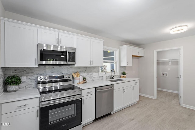 kitchen with a sink, appliances with stainless steel finishes, decorative backsplash, and light wood-type flooring