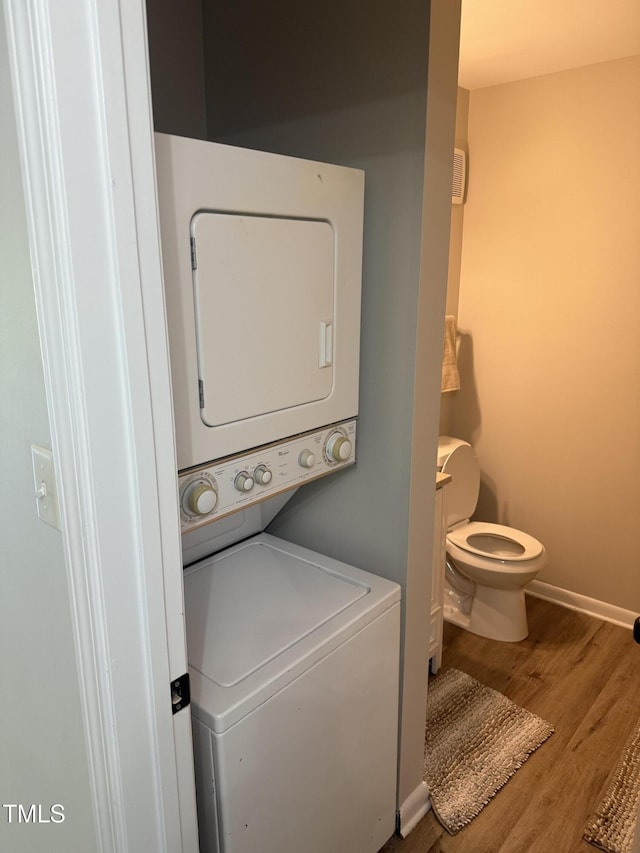 laundry area featuring stacked washer / dryer, laundry area, wood finished floors, and baseboards