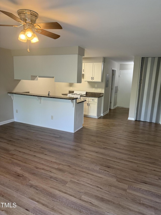 kitchen with a kitchen breakfast bar, white cabinetry, dark countertops, baseboards, and a ceiling fan