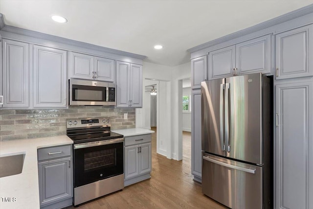 kitchen featuring decorative backsplash, light countertops, gray cabinets, light wood-style flooring, and stainless steel appliances