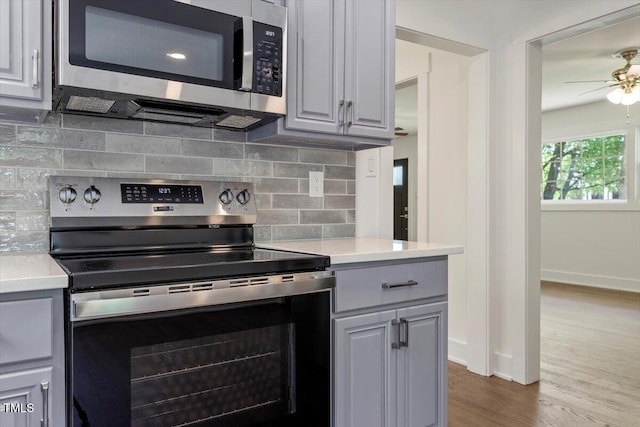 kitchen featuring a ceiling fan, appliances with stainless steel finishes, tasteful backsplash, wood finished floors, and light countertops