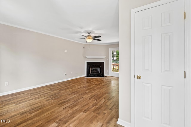 unfurnished living room featuring crown molding, a ceiling fan, baseboards, a fireplace with flush hearth, and wood finished floors