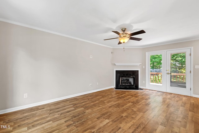 unfurnished living room featuring a ceiling fan, a fireplace with flush hearth, wood finished floors, baseboards, and ornamental molding