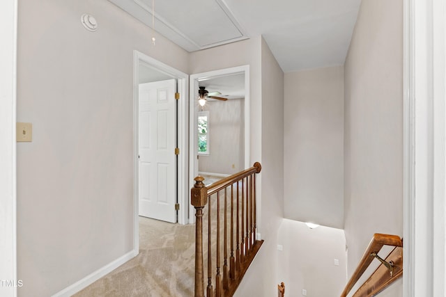 hallway featuring carpet flooring, baseboards, an upstairs landing, and attic access