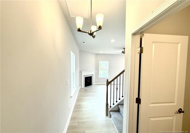 hallway featuring visible vents, baseboards, an inviting chandelier, light wood finished floors, and stairs