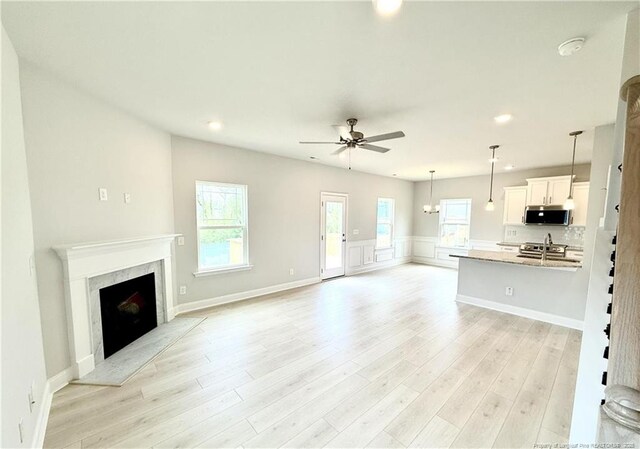 unfurnished living room with a healthy amount of sunlight, ceiling fan, and light wood-style flooring