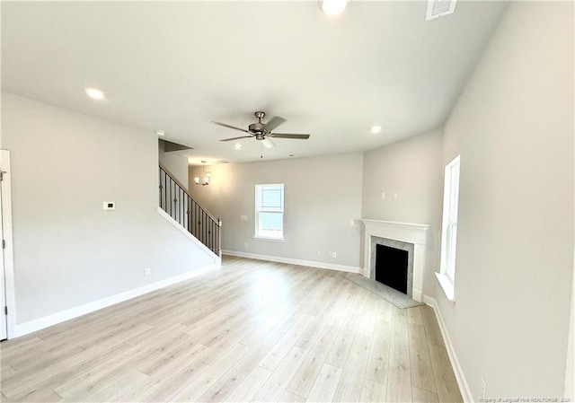 unfurnished living room with stairway, light wood finished floors, a fireplace, visible vents, and a ceiling fan