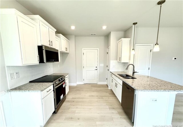 kitchen with light stone countertops, appliances with stainless steel finishes, a sink, light wood-type flooring, and a peninsula
