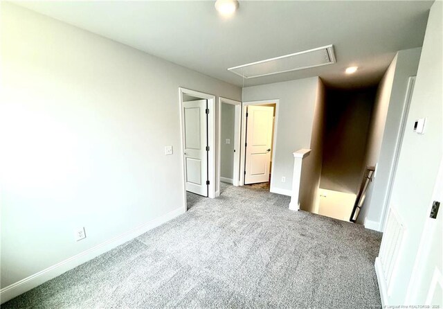 unfurnished bedroom with attic access, visible vents, carpet floors, and baseboards
