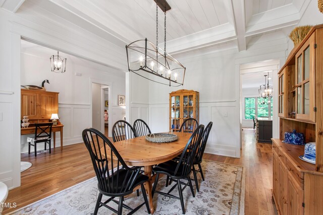 197 Boxwood Dr, Pittsboro, NC 27312 - dining space featuring a chandelier, beam ceiling, light wood-type flooring, a decorative wall, and a wainscoted wall