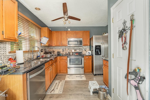 kitchen with dark countertops, a sink, light wood-type flooring, ceiling fan, and appliances with stainless steel finishes