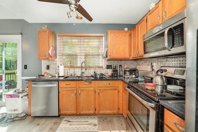 kitchen featuring a sink, light wood-type flooring, ceiling fan, backsplash, and appliances with stainless steel finishes