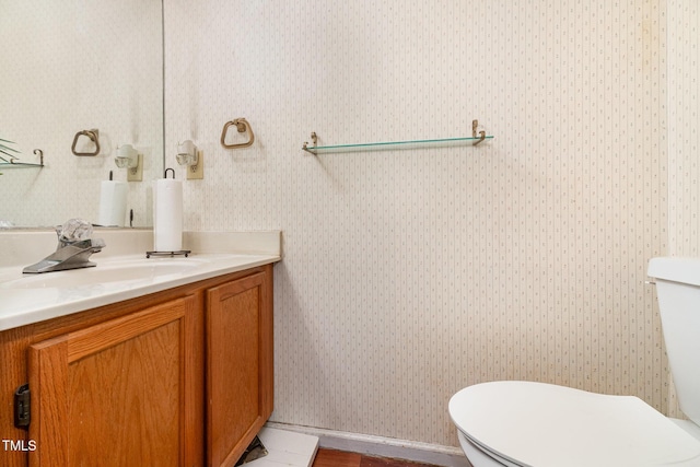 bathroom with toilet, vanity, and wallpapered walls