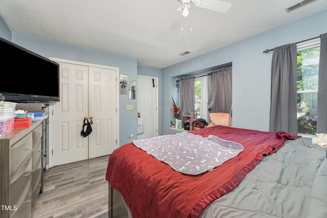 bedroom with visible vents, a textured ceiling, light wood-style floors, and a closet