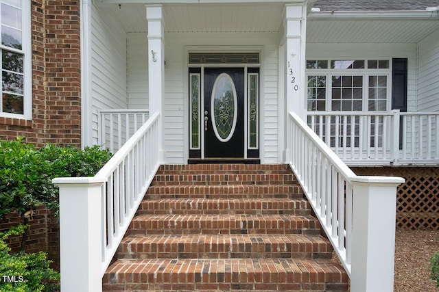 property entrance featuring a porch, a shingled roof, and brick siding