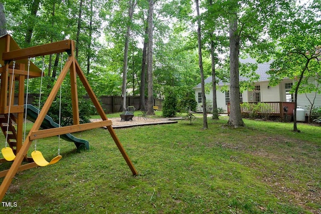 view of yard with a deck, a playground, a fenced backyard, and an outdoor fire pit