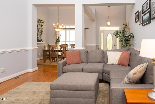 living area with wood finished floors, an inviting chandelier, baseboards, visible vents, and lofted ceiling