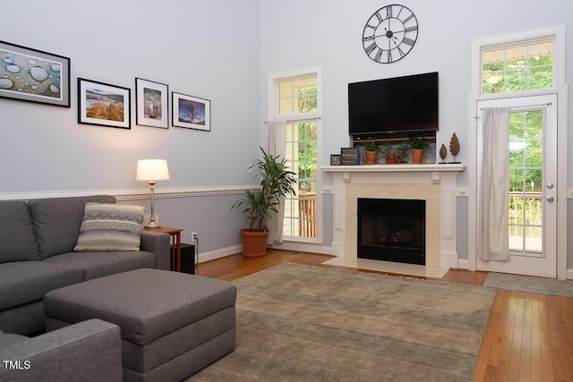 living room featuring a towering ceiling, hardwood / wood-style floors, a high end fireplace, and baseboards