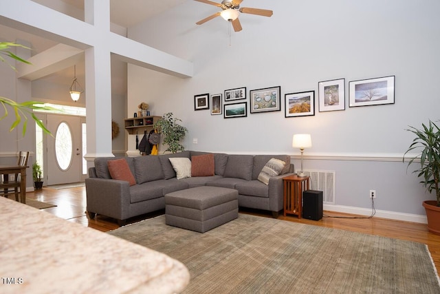 living room featuring ceiling fan, visible vents, baseboards, a towering ceiling, and wood finished floors