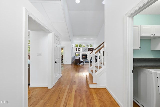 hallway featuring baseboards, light wood finished floors, washer / clothes dryer, and stairs