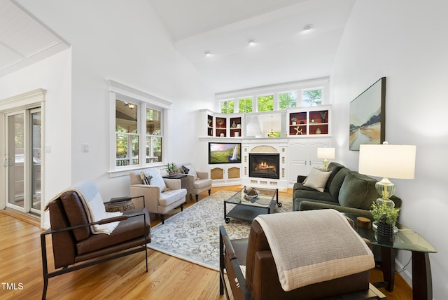 living room with high vaulted ceiling, a warm lit fireplace, and wood finished floors