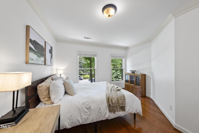 bedroom with baseboards, ornamental molding, wood finished floors, and visible vents