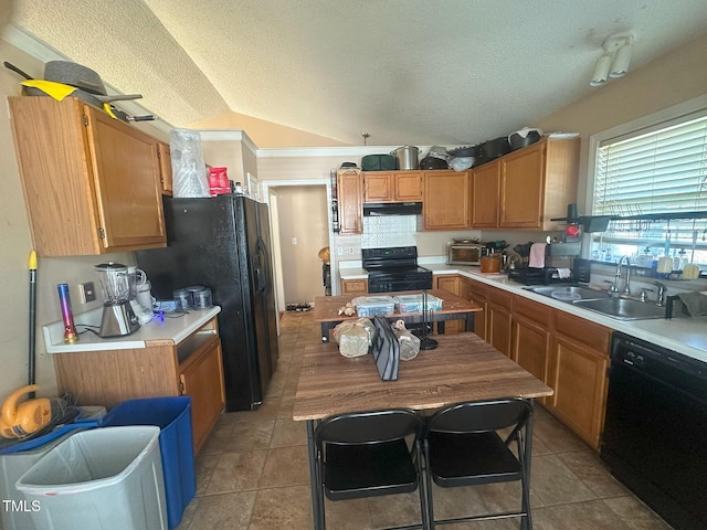 kitchen with light countertops, under cabinet range hood, a sink, black appliances, and vaulted ceiling