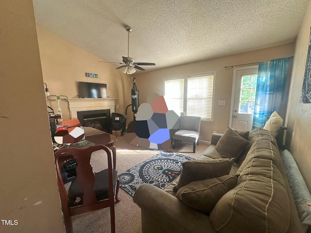 living room featuring a glass covered fireplace, carpet, a ceiling fan, and a textured ceiling
