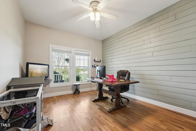 office area featuring baseboards, ceiling fan, wood finished floors, and wooden walls
