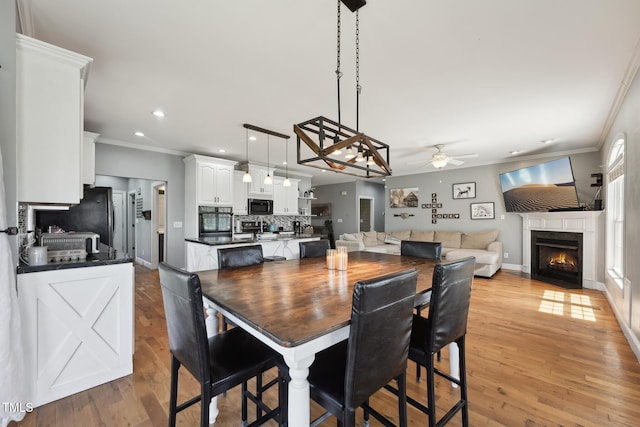 dining room featuring crown molding, ceiling fan, a fireplace with flush hearth, and light wood-style floors