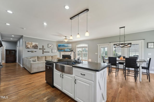 kitchen with a warm lit fireplace, dark countertops, ornamental molding, and a sink