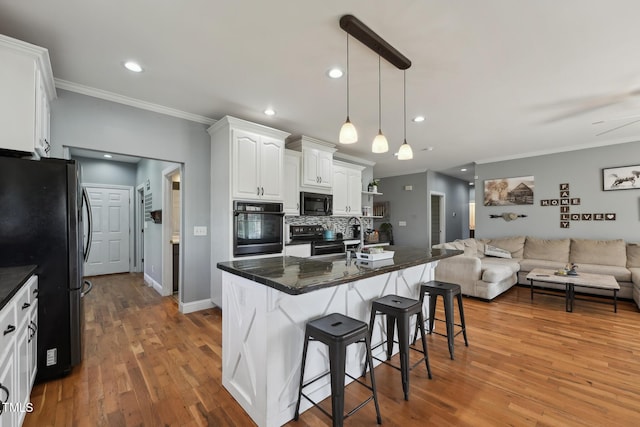 kitchen with crown molding, a breakfast bar, black appliances, and open floor plan