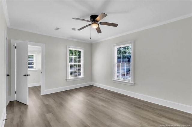 empty room with wood finished floors, visible vents, a ceiling fan, crown molding, and baseboards