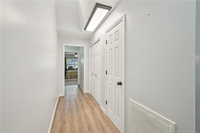 hall featuring light wood finished floors, baseboards, and visible vents