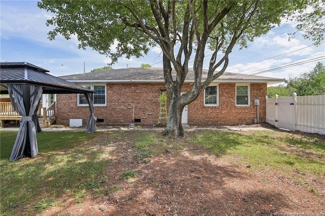 rear view of house with a gate, a gazebo, crawl space, a lawn, and brick siding