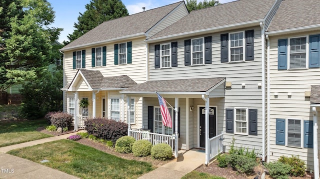 view of property with a shingled roof, a porch, and a front lawn