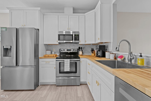 kitchen with a sink, appliances with stainless steel finishes, butcher block counters, and white cabinetry